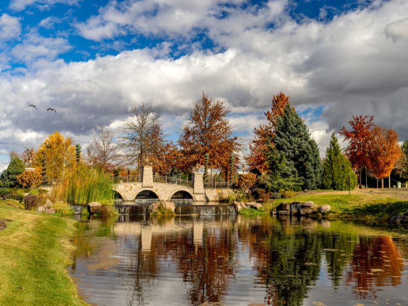 Scenic view of a charming stone bridge over a peaceful pond in Eagle, Idaho, surrounded by vibrant autumn trees and lush greenery. With CBH Homes' new Beaconwood community coming to this desirable location, homebuyers can enjoy stunning natural beauty, top-rated schools, and a thriving lifestyle. Discover your dream home in Eagle, ID with CBH Homes today!